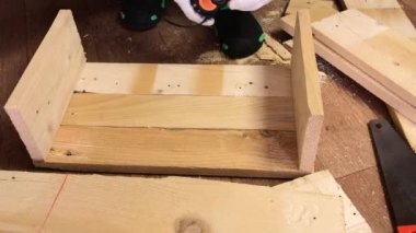 Boyutları mezurayla ölçüyor, tahtalara testere çizgileri çiziyor. Sebze toplamak için bir depolama kutusu yapıyor. Bir apartman dairesinde salgın sırasında sebze toplamak..