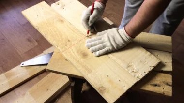 Adam testere tahtalarını dener ve kırmızı kalemle kesme çizgisini işaretler. Sebze toplamak için bir depolama kutusu yapıyor. Bir apartman dairesinde salgın sırasında sebze toplamak.