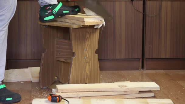 Un homme scie une planche avec une scie à métaux. Fait une boîte de stockage pour la récolte des légumes. Récolte de légumes pendant l'épidémie dans un appartement de la ville — Video