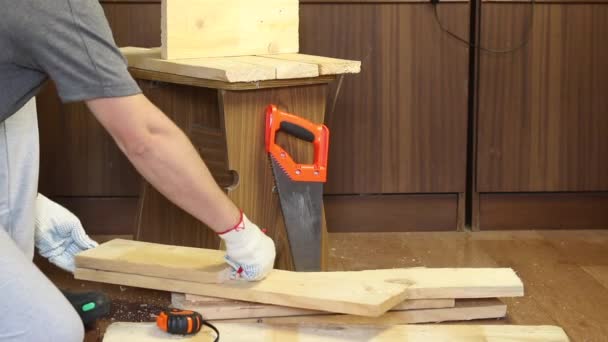 De man tekent met een potlood snijlijnen op de planken. Maakt een opbergdoos voor het oogsten van groenten. Groenten oogsten tijdens de epidemie in een stadsappartement. — Stockvideo