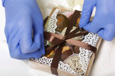 Lastik eldivenli bir kadın karton bir kutuyu kurutulmuş meyve ve fındık şekeriyle bantlıyor. Salgın sırasında kendini izole ederek evde yapılmış..