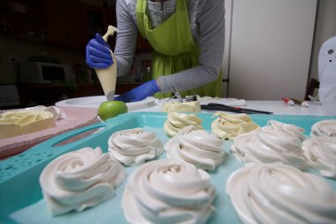 Lastik eldivenli bir kadın, pasta çantalı bir zephyr oluşturur. Taze şekerlemeler tepsinin üzerinde. Salgın sırasında tatlı pişirmek.