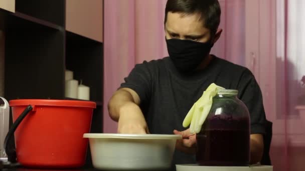 Muž v lékařské masce používá ruce k hnětení modrých hroznů odebraných z bandy. Výroba domácího vína během epidemie. — Stock video