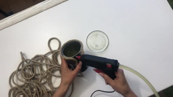 A woman wraps a rope around a tin can. Fastens the rope with a glue gun. Crafts in self-isolation. Filmed from above. — Stock Video