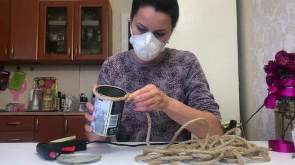 En kvinna i respirator lindar en tryckförband runt en plåtburk. Fäst tryckförrådet med limpistol. Självisolerande hantverk — Stockvideo