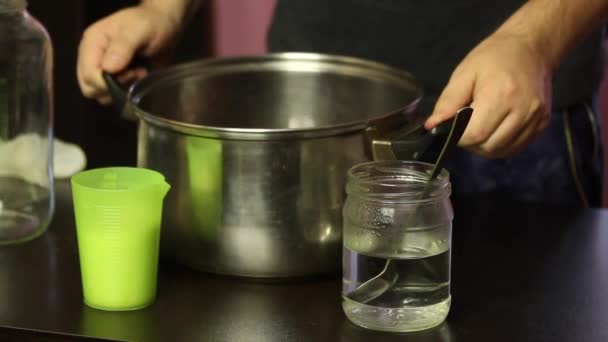 Een man met een medisch masker giet geperst druivensap in een glazen pot. Zelfgemaakte wijn maken tijdens een epidemie.. — Stockvideo