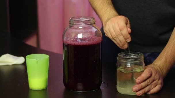 De man lost suiker op in water en voegt toe aan druivensap. Zelfgemaakte wijn maken tijdens een epidemie. Close-up. — Stockvideo