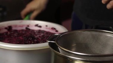 Adam süzgeçten üzüm hamuru süzüyor. Meyve suyunu ayırır. Salgın sırasında ev yapımı şarap yapmak. Yan görünüm.