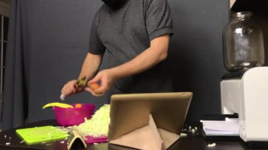 Tıbbi maskeli bir adam havuç soyardı. Yakında doğranmış lahana var. Süreci video bağlantısı ile yayınlar. Salgın sırasında evde lahana turşusu.