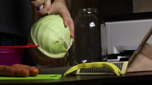 Un hombre transmite el proceso de cortar la col a través de un enlace de vídeo. Sauerkraut en casa. En la mesa junto a él hay repollo, zanahorias y utensilios de cocina. Primer plano de disparo — Vídeos de Stock