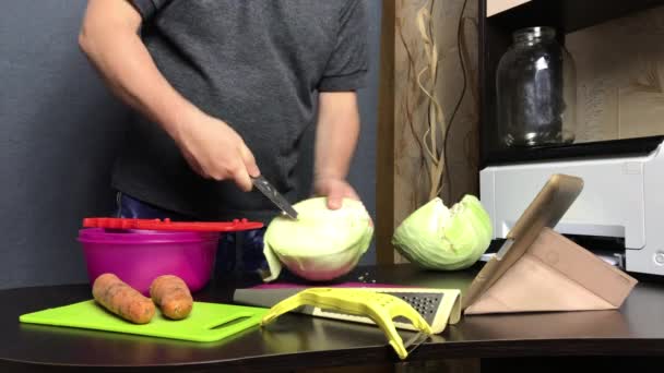 एक माणूस व्हिडिओ लिंकद्वारे केबज चिरण्याची प्रक्रिया प्रसारित करतो. घरात सॉरक्रॉट. त्याच्या पुढील टेबलावर कोबी, गाजर आणि स्वयंपाक साधने आहेत . — स्टॉक व्हिडिओ