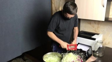 Tıbbi maskeli bir adam lahana doğrayıp tencereye koyar. Öğütme işlemini video bağlantısı ile yayınlar. Salgın sırasında evde lahana turşusu.