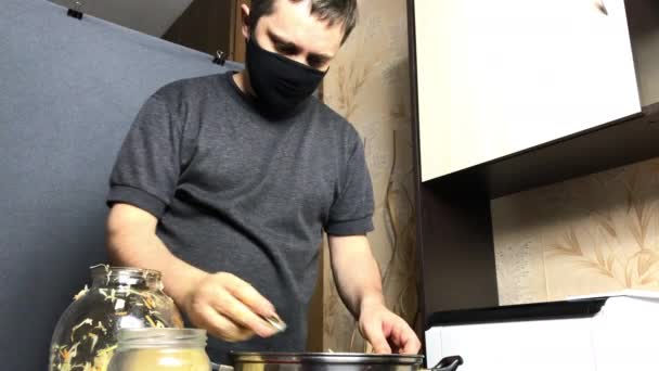 Человек в медицинской маске льет семена укропа в измельченную капусту. Соус дома во время пандемии. — стоковое видео