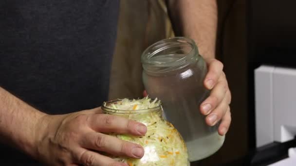 Un hombre vierte agua y sal en un frasco de col picada. Sauerkraut en casa durante una pandemia. Primer plano de disparo. — Vídeos de Stock