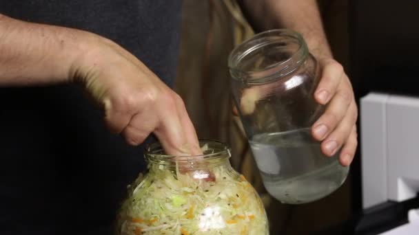 Un homme verse de l'eau et du sel dans un bocal de chou haché. Joints avec les doigts. Choucroute à la maison pendant une pandémie. Gros plan. — Video