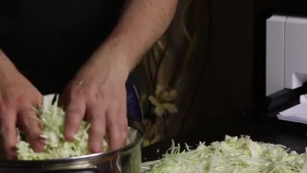 Ein Mann legt zerfetztes Kohl in einen Topf. Sauerkraut zu Hause während einer Pandemie. Nahaufnahme. — Stockvideo