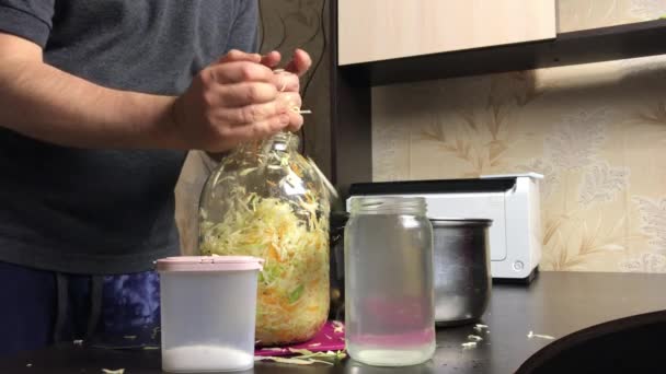 Ein Mann legt zerfetztes Kohl in ein Glas. Mit einem Nudelholz verschließen. Sauerkraut zu Hause während einer Pandemie. — Stockvideo