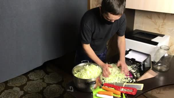 A man wearing a medical mask puts chopped cabbage into a saucepan. Broadcasts the grinding process via video link. Sauerkraut at home during a pandemic — Stock Video