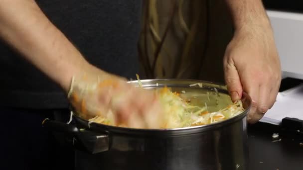 El hombre se mezcla con sus manos y amasa la col picada y las zanahorias en una cacerola. Sauerkraut en casa durante una pandemia. — Vídeos de Stock