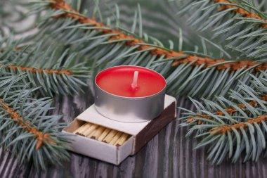 Çam ağaçlarının üzerinde mavi ladin dalları. Yakınlarda bir mum ve bir kutu kibrit var..