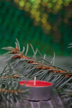 Çam ağaçlarının üzerinde mavi ladin dalları. Yakınlarda kırmızı bir mum var. Arkaplan, yeşilin yanardöner bir yüzeyi. Yakın çekim..