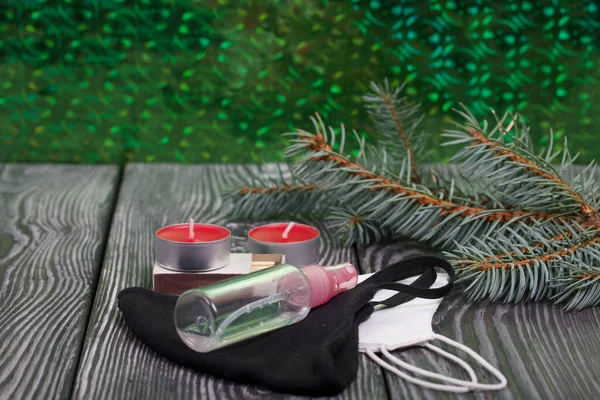 Branches of blue spruce on pine boards. Nearby are red candles, medical masks and an antiseptic. Close-up shot.