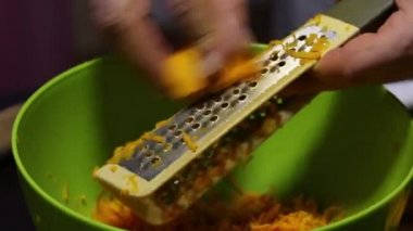 Adamın biri rendeleyiciye balkabağı parçaları sürüyor. Balkabağı talaşları bir kabın içine konur. Yan taraftan yakın çekim..