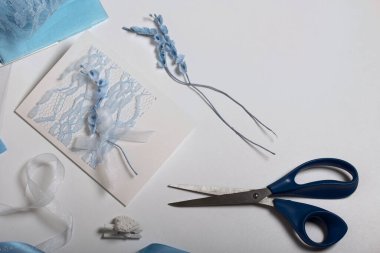 Tebrik kartları hazırlıyorum. Masanın beyaz yüzeyinde el işi aksesuarlar. Kurumuş çiçekler ve el işleri için kurdeleler. Yaratıcılık için araçlar.