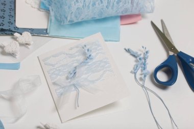 Tebrik kartları hazırlıyorum. Masanın beyaz yüzeyinde el işi aksesuarlar. Kurumuş çiçekler ve el işleri için kurdeleler. Yaratıcılık için araçlar.