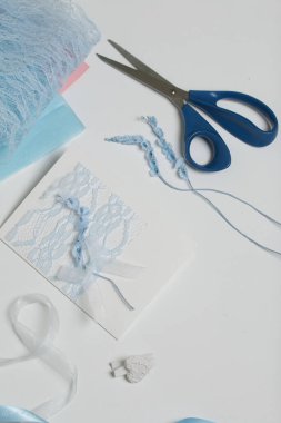 Tebrik kartları hazırlıyorum. Masanın beyaz yüzeyinde el işi aksesuarlar. Kurumuş çiçekler ve el işleri için kurdeleler. Yaratıcılık için araçlar.