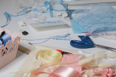 Tebrik kartları hazırlıyorum. Masanın beyaz yüzeyinde el işi aksesuarlar. Kurumuş çiçekler ve el işleri için kurdeleler. Yaratıcılık için araçlar.