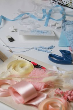 Tebrik kartları hazırlıyorum. Masanın beyaz yüzeyinde el işi aksesuarlar. Kurumuş çiçekler ve el işleri için kurdeleler. Yaratıcılık için araçlar.