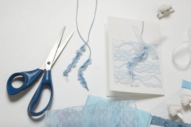 Tebrik kartları hazırlıyorum. Masanın beyaz yüzeyinde el işi aksesuarlar. Kurumuş çiçekler ve el işleri için kurdeleler. Yaratıcılık için araçlar.