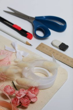 İğne işi aksesuarlar. Kurumuş çiçekler ve el işleri için kurdeleler. Yaratıcılık için araçlar. Beyaz bir masanın üstünde.