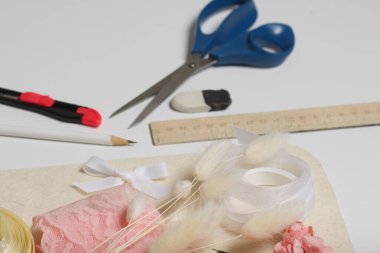 İğne işi aksesuarlar. Kurumuş çiçekler ve el işleri için kurdeleler. Yaratıcılık için araçlar. Beyaz bir masanın üstünde.