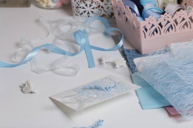 Tebrik kartları hazırlıyorum. Masanın beyaz yüzeyinde el işi aksesuarlar. Kurumuş çiçekler ve el işleri için kurdeleler. Yaratıcılık için araçlar.