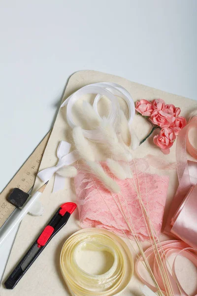 İğne işi aksesuarlar. Kurumuş çiçekler ve el işleri için kurdeleler. Yaratıcılık için araçlar. Beyaz bir masanın üstünde.