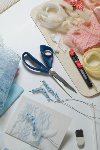 Tebrik kartları hazırlıyorum. Masanın beyaz yüzeyinde el işi aksesuarlar. Kurumuş çiçekler ve el işleri için kurdeleler. Yaratıcılık için araçlar.