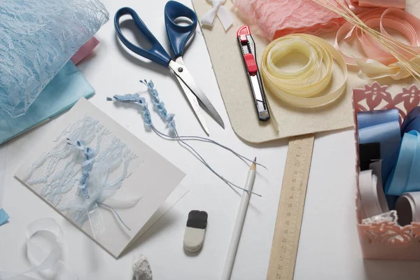 Tebrik kartları hazırlıyorum. Masanın beyaz yüzeyinde el işi aksesuarlar. Kurumuş çiçekler ve el işleri için kurdeleler. Yaratıcılık için araçlar.