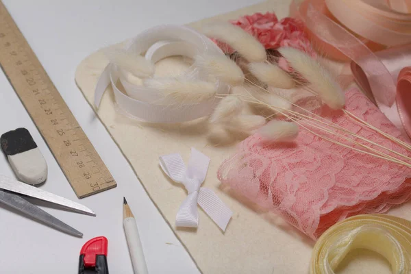 İğne işi aksesuarlar. Kurumuş çiçekler ve el işleri için kurdeleler. Yaratıcılık için araçlar. Beyaz bir masanın üstünde.