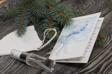 Tebrik kartı, tıbbi maske ve antiseptik. Ladin dallarının arasında. Siyah çam ağaçlarının üzerinde yatıyorlar..