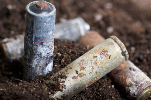 Corroded batteries covered with earth. Environmental protection and waste recycling. Close-up shot.