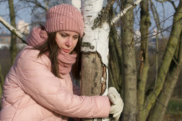 A girl in autumn clothes stands next to a birch tree. Walking in nature in the park.