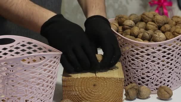 Un uomo punge le noci con un martello. Su un blocco di legno. Separa le conchiglie e i gherigli e li inserisce nel cesto. Quelli viziati vengono gettati nell'urna. Primo piano. — Video Stock