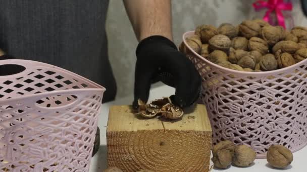 Un uomo punge le noci con un martello. Su un blocco di legno. Separa le conchiglie e i gherigli e li inserisce nel cesto. Quelli viziati sono gettati nell'urna. — Video Stock