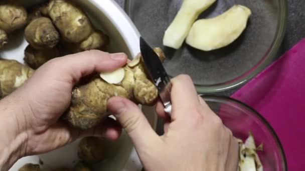 Muž oloupe jeruzalémský artyčok kuchyňským nožem. Hodí slupku do jedné nádoby, loupaná zelenina do druhé. Detailní záběr shora. — Stock video
