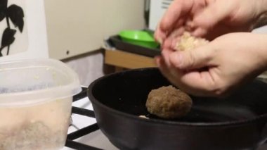 Adam pirzola kızartıyor. Konteynırdan kıyma alıp topları yuvarlıyor. Onları kızgın tavaya koyuyor. Yakın çekim.