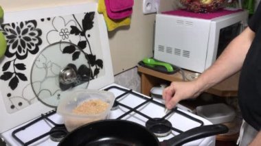 Adam pirzola hazırlıyor. Gaz sobasında ateş yakar. Tavayı ateşe koyar, içine yağ döker. Yakınlarda kıymalı bir kap var..