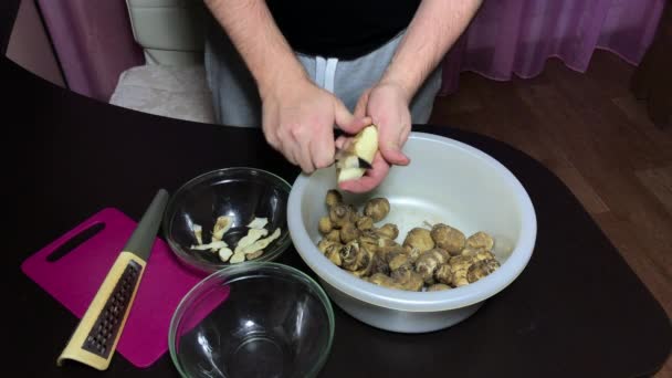 Um homem descasca alcachofra de Jerusalém com uma faca. Solta o vegetal descascado em um recipiente, a casca em outro — Vídeo de Stock