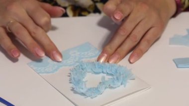 Bir kadın masaya oturur ve tebrik kartı hazırlar. Kağıda dantel bant yapıştırıyor. Yakın çekim..